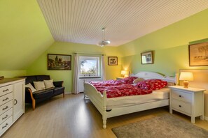 Une chambre à coucher comprenant un lit, une table de chevet, une commode, une fenêtre et un ventilateur de plafond.