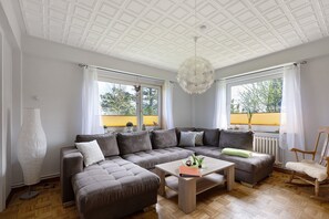 A modern living room with a sectional sofa, a coffee table, and a rocking chair. - Apartment 'Ebbe' with Shared Garden and Wi-Fi (Hallig Langeneß)