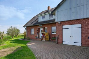 A brick house with a paved driveway, a garage door, and a small porch area. - Apartment 'Ebbe' with Shared Garden and Wi-Fi (Hallig Langeneß)