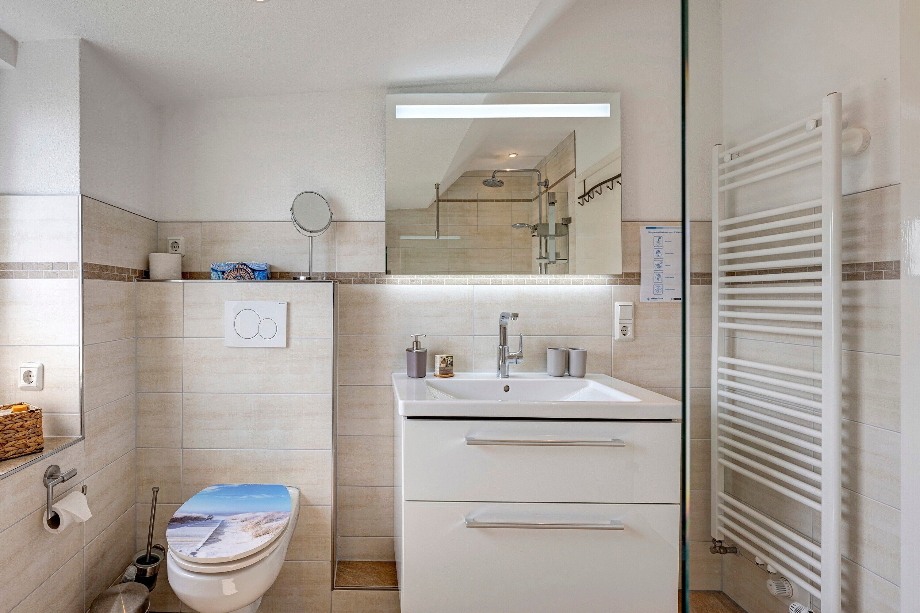 Een moderne badkamer met toilet, wastafel, spiegel en handdoekhouder.