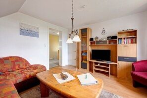 A living room with a sofa, a wooden coffee table, a television, and a bookshelf.