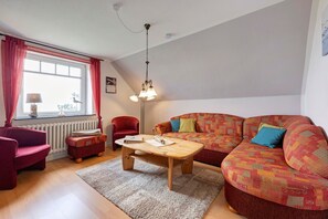 A cozy living room with a wooden coffee table, a red sofa, a red armchair, and a patterned sofa.