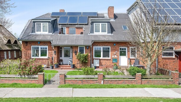 Una casa de dos pisos con paneles solares, fachada de ladrillo y un jardín delantero.