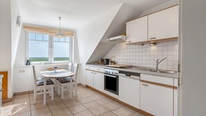 Una cocina con armarios blancos, estufa, fregadero y una mesa de comedor con sillas.