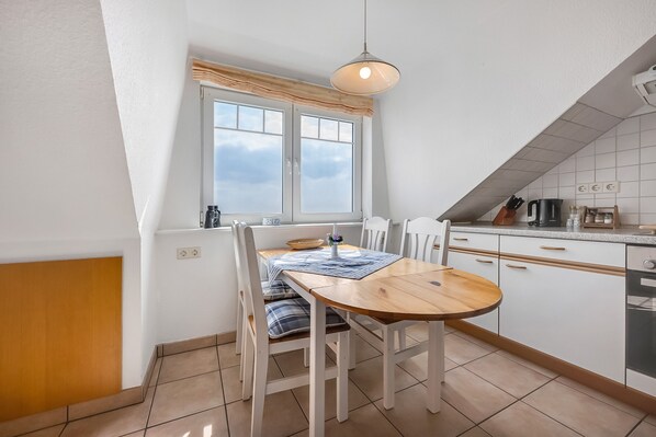 Une cuisine avec une table à manger, des chaises, une fenêtre et un luminaire suspendu.