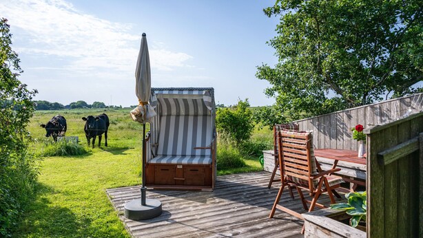 A wooden deck with a striped chair and table, a small round table, and a view of cows in the background. - Apartment 'Ferienwohnung Voglkoje' with Private Terrace, Shared Garden and Wi-Fi (Pellworm)