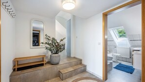 A modern interior with a wooden bench, a large potted plant, and a staircase leading to a bathroom with a skylight. - Apartment 'Ferienwohnung Voglkoje' with Private Terrace, Shared Garden and Wi-Fi (Pellworm)