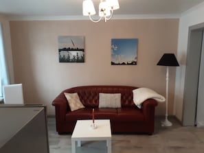 A living room with a brown leather sofa, a white coffee table, and two wall-mounted paintings. - Apartment 'Das Weiße Stadthaus' with Wi-Fi (Wesselburen)