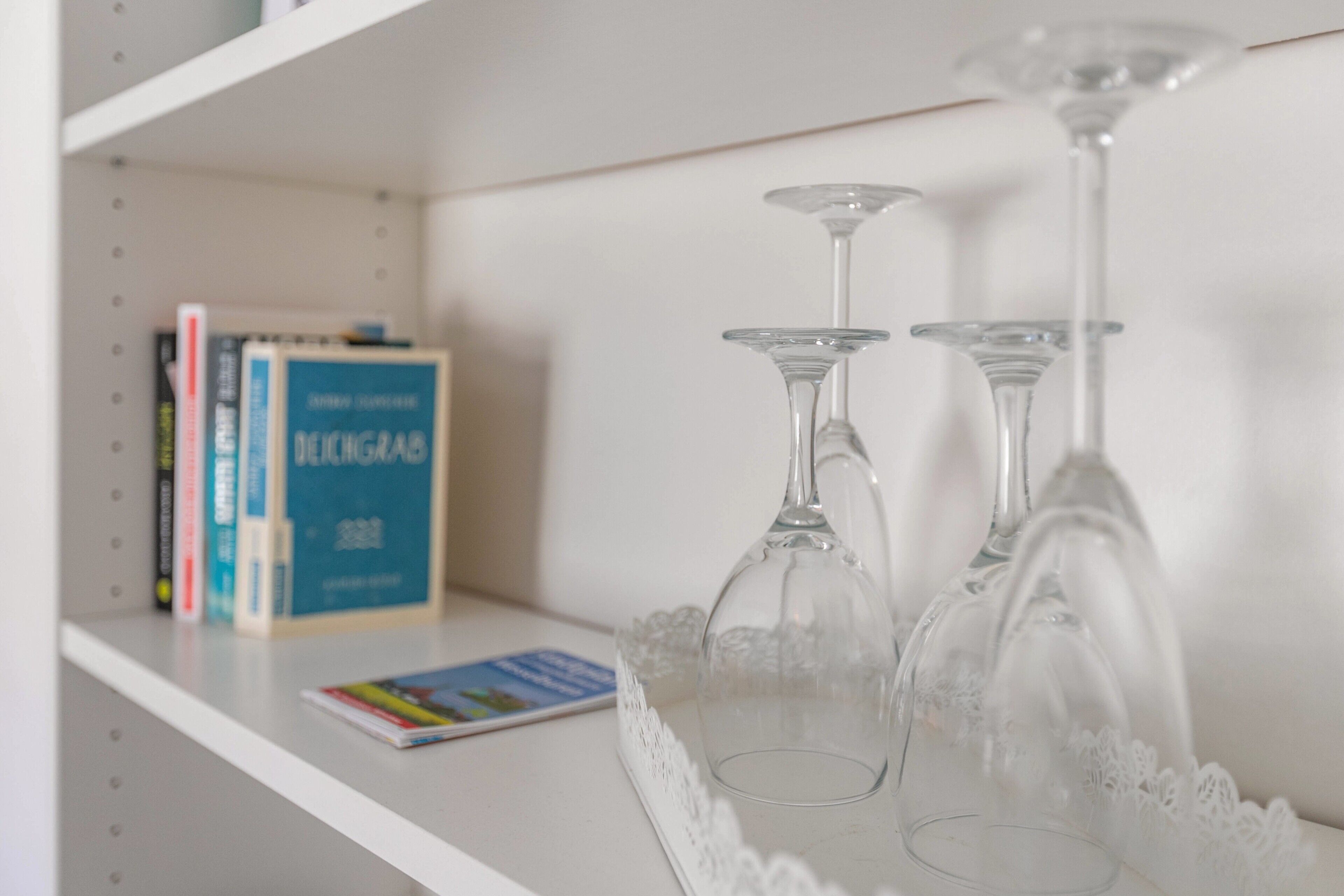 Una libreria con libri e due bicchieri di vetro trasparente per il vino su uno scaffale bianco.
