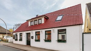 Un edificio blanco con techo rojo, varias ventanas y una estructura pequeña adosada.