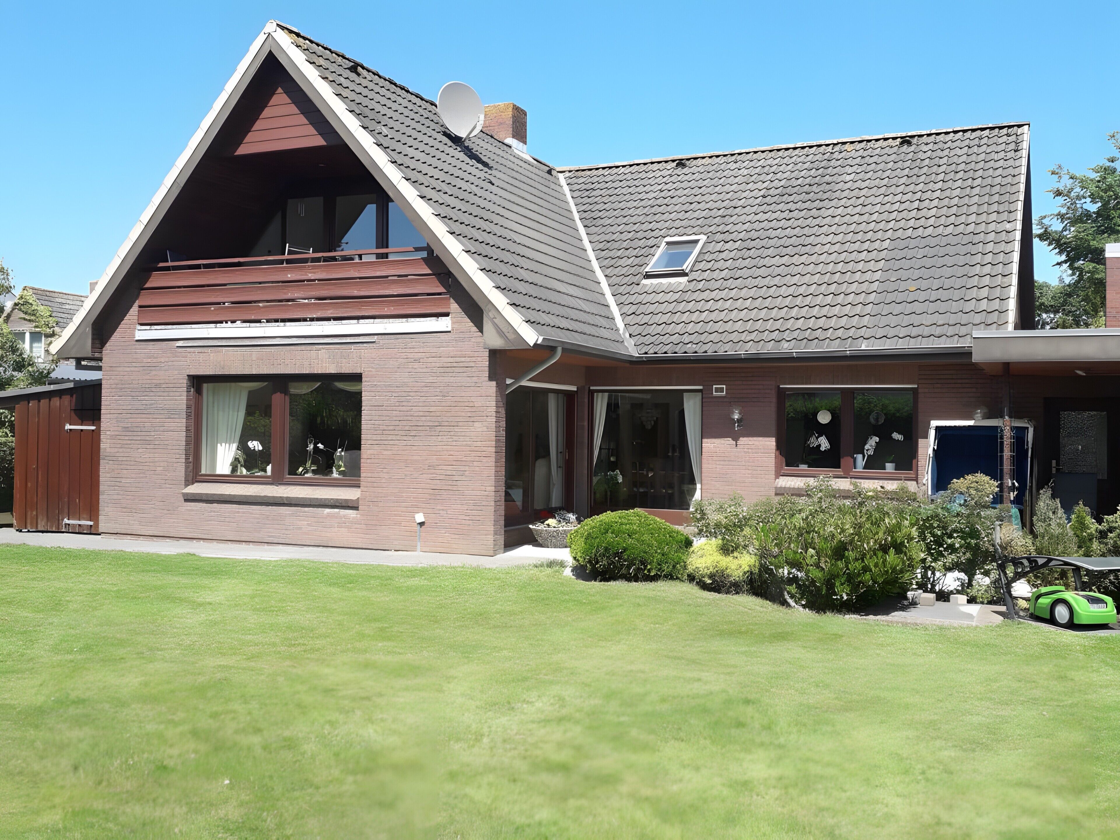 Ein zweistöckiges Haus mit geneigtem Dach, großen Fenstern und einer sichtbaren Satellitenschüssel.