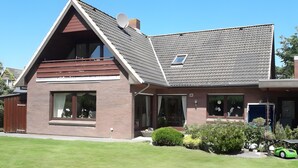 Ein zweistöckiges Haus mit geneigtem Dach, großen Fenstern und einer sichtbaren Satellitenschüssel.