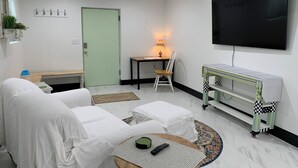 Une pièce moderne et bien éclairée, comprenant un canapé, une petite table, une chaise, un téléviseur et un chariot.