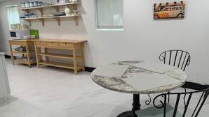 Un coin repas comprenant une table ronde, deux chaises, une console en bois avec des étagères et un four à micro-ondes.