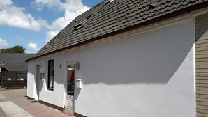 A white building with a tiled roof, a door, and a small window. - Apartment 'Ferienwohnung Edel' with Private Terrace and Wi-Fi (Wesselburen)