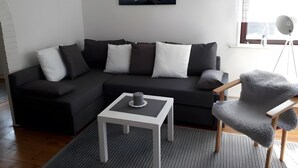A modern living room with a dark sofa, a small white table, a fluffy chair, and a painting on the wall. - Apartment 'Ferienwohnung Edel' with Private Terrace and Wi-Fi (Wesselburen)