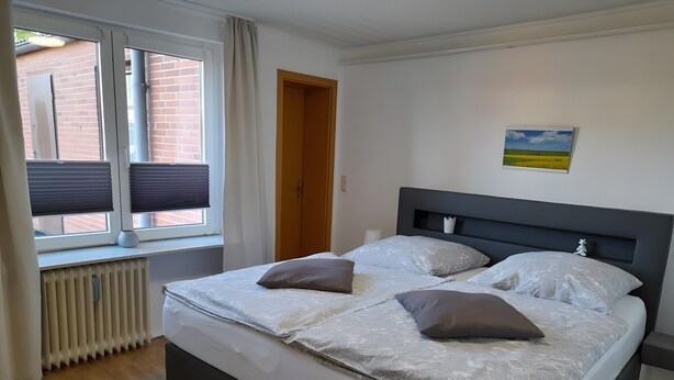 A bedroom with a bed, a radiator, a window with blinds, a door, and a wall-mounted picture. - Apartment 'Ferienwohnung Edel' with Private Terrace and Wi-Fi (Wesselburen)