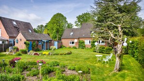 A residential garden with a lawn, a tree, and a small white table and chairs. - Apartment 'Halunder' with Private Garden and Wi-Fi (Leck)