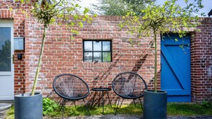A brick building with a blue door, two outdoor chairs, and potted plants. - Apartment 'Halunder' with Private Garden and Wi-Fi (Leck)