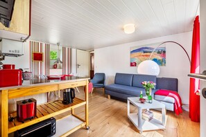Un espacio habitable compacto con kitchenette, un sofá, una mesa de comedor y un cuadro en la pared.