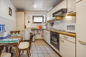 Cozinha compacta com mesa, cadeiras, micro-ondas, fogão e janela com cortina.