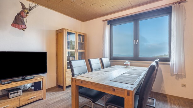 A dining area with a wooden table, chairs, a television on a stand, and a bookshelf. - Apartment 'Fernblick, 83 sqm' with Shared Terrace, Garden, and Wi-Fi (Bad Grund)