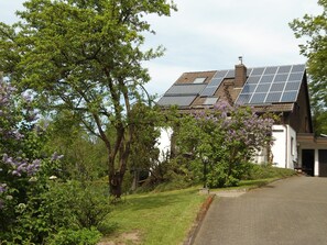 Una casa con paneles solares en el techo, rodeada de vegetación y árboles.