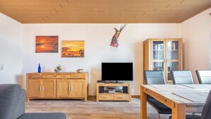 A living room with a wooden cabinet, TV, and a dining table with chairs. - Apartment 'Fernblick, 83 sqm' with Shared Terrace, Garden, and Wi-Fi (Bad Grund)