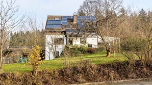 A house with solar panels on the roof, surrounded by trees and a grassy area. - Apartment 'Fernblick, 83 sqm' with Shared Terrace, Garden, and Wi-Fi (Bad Grund)