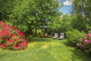 Un jardin agrémenté d’un kiosque, de deux chaises et de fleurs en pleine floraison.