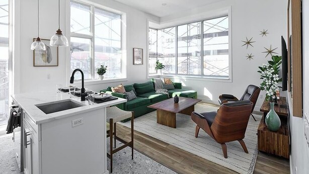 A modern living room with a green sofa, wooden coffee table, and a kitchen area with a sink and countertop.