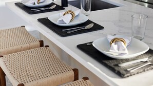 A modern kitchen with a white marble countertop, black placemats, and woven chairs.