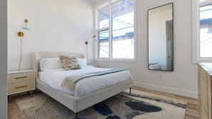 A bedroom with a bed, bedside tables, a large window, and a mirror.