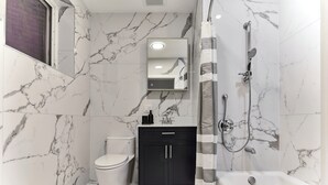 A bathroom with a toilet, a black cabinet, a mirror, and a shower area. - Bright Cozy Loft | Walk to PATH Shops + Dining (Hoboken)