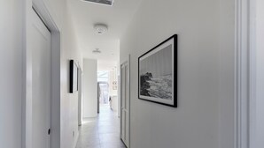 A hallway with white walls, a framed black and white photograph, and a door at the end. - Bright Cozy Loft | Walk to PATH Shops + Dining (Hoboken)