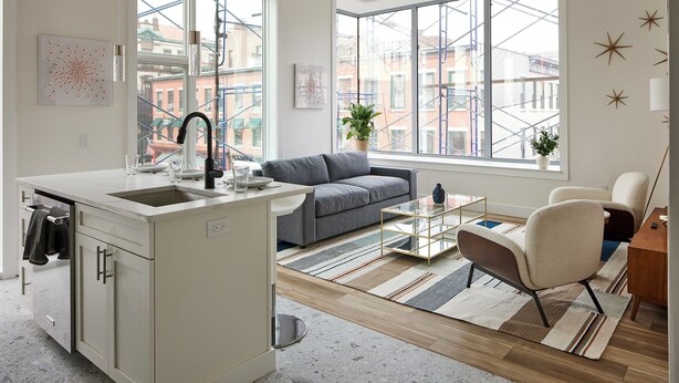 A modern kitchen with a built-in island, a gray sofa, and a glass coffee table. - Bright Cozy Loft | Walk to PATH Shops + Dining (Hoboken)