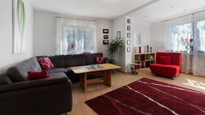Ett vardagsrum med en soffa, en röd fåtölj, ett soffbord och en röd matta.