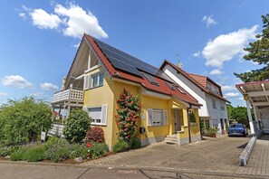 A yellow house with a red roof, solar panels, and a garden with flowers. - Apartment 'Lavendel' with Balcony and Wi-Fi (Ringsheim)