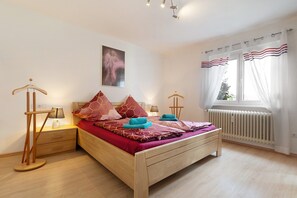 Ein Schlafzimmer mit einem hölzernen Bett, einem Nachttisch mit Lampe, einem Heizkörper und einem Fenster mit Vorhängen.