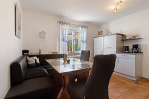 Ein Essbereich mit Holztisch, schwarzem Ledersofa und einer Küche mit weißen Schränken sowie einer Kaffeemaschine.