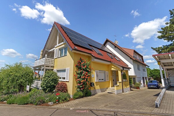 A yellow house with a red roof, solar panels, and a garden with flowers.