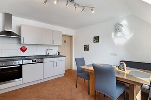 A modern kitchen with white cabinets, a built-in oven, and a dining area with a wooden table and chairs.