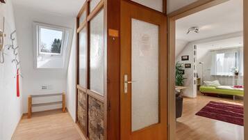 Ein Zimmer mit Holztür, kleinem Fenster, Heizkörper, Bett und einer Pflanze.