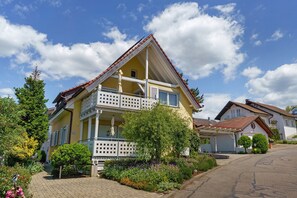 A two-story house with a balcony, surrounded by a garden with various plants and flowers.