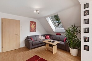 A modern living room with a sectional sofa, a wooden coffee table, a large potted plant, and a skylight.