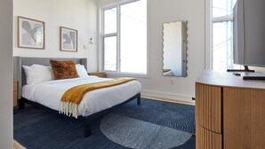 A bedroom with a bed, a dresser, a large window, and two wall-mounted artworks. - Bright Designer Loft  –  steps from PATH to NYC (Hoboken)