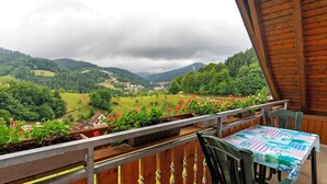 A balcony with a table and chairs, overlooking a valley with houses and greenery. - Ferienhof Brutoni Apartment "Schwarzwaldtraum" with Mountain View, Balcony, Shared BBQ Area (Bad Peterstal-Griesbach)