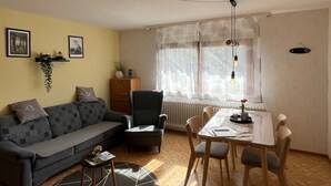 A living room with a sofa, armchair, dining table, and a patterned rug. - Ferienhof Brutoni Apartment "Schwarzwaldtraum" with Mountain View, Balcony, Shared BBQ Area (Bad Peterstal-Griesbach)