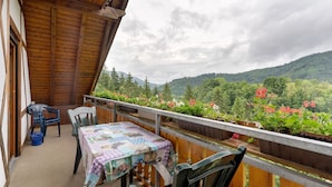 Un balcon doté d’un plafond en bois, une table recouverte d’une nappe matelassée et une vue sur une chaîne de montagnes boisée.