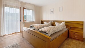 Une chambre à coucher avec un lit en bois, une table de chevet, une fenêtre avec des rideaux et un radiateur.